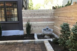 Custom back area of a home with paver patio, stone planters, and cedar wood fence.